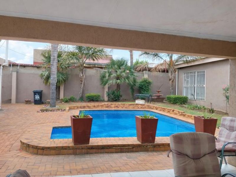 Outdoor pool area featuring a paved patio, built-in braai, and a swimming pool set within a private, walled garden space.