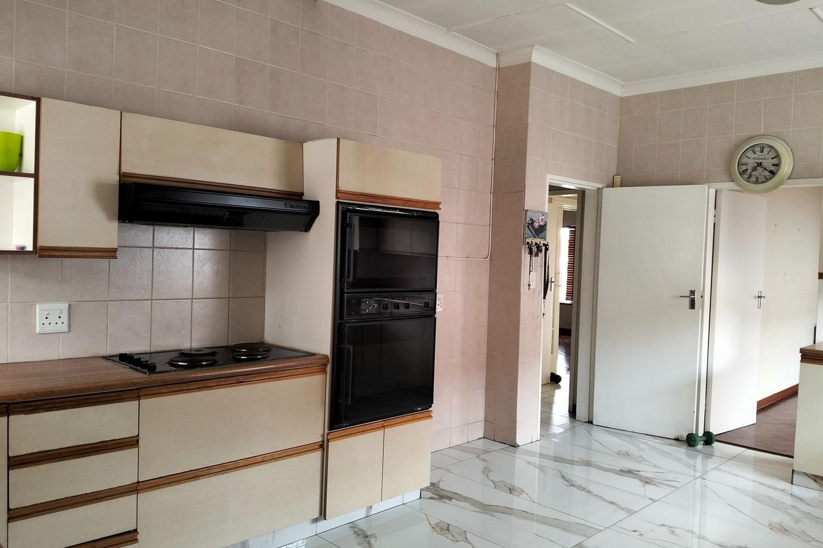 A functional kitchen featuring built-in cabinetry, an integrated double oven, electric hob, extractor fan, and modern marble-look floor tiles.