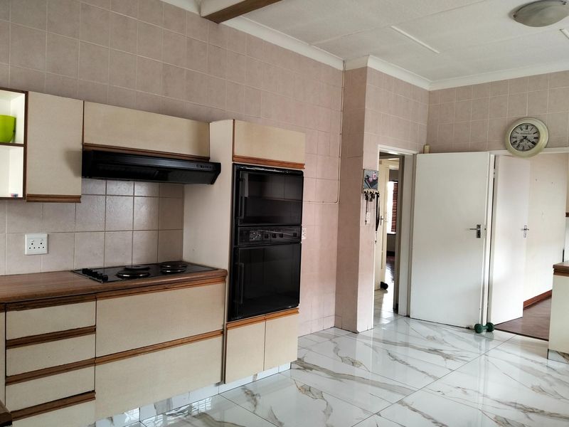 A functional kitchen featuring built-in cabinetry, an integrated double oven, electric hob, extractor fan, and modern marble-look floor tiles.