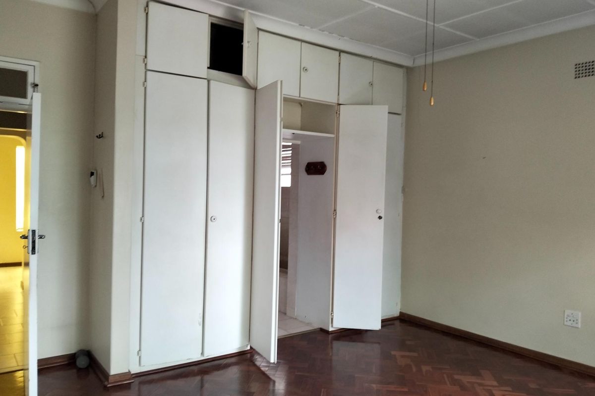 A spacious bedroom featuring classic parquet flooring, built-in cupboards with overhead storage, and a ceiling fan.