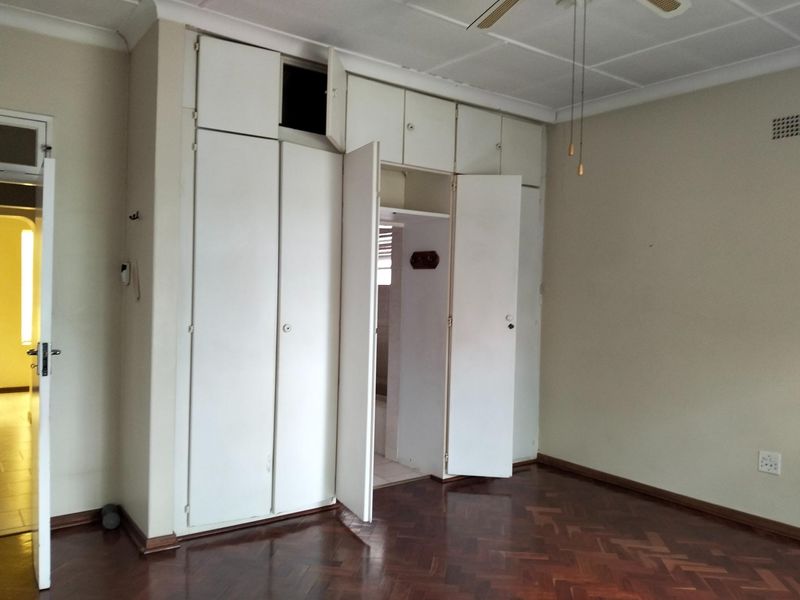 A spacious bedroom featuring classic parquet flooring, built-in cupboards with overhead storage, and a ceiling fan.