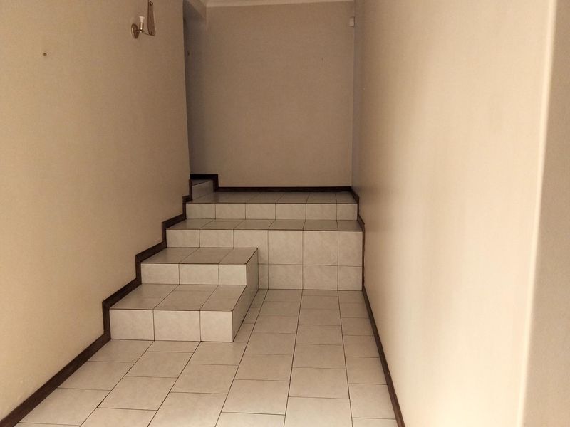 A simple, tiled hallway featuring a small staircase leading to an upper level, finished with neutral wall paint and basic lighting.