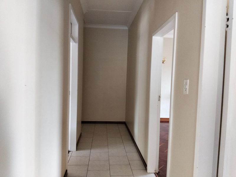 A clean, neutral-toned hallway featuring tiled flooring and multiple doorways leading to adjacent rooms.