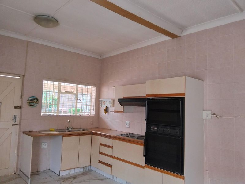 A dated kitchen featuring built-in cabinetry, a double sink, integrated oven, and hob, with tiled splashbacks and security bars on the window.