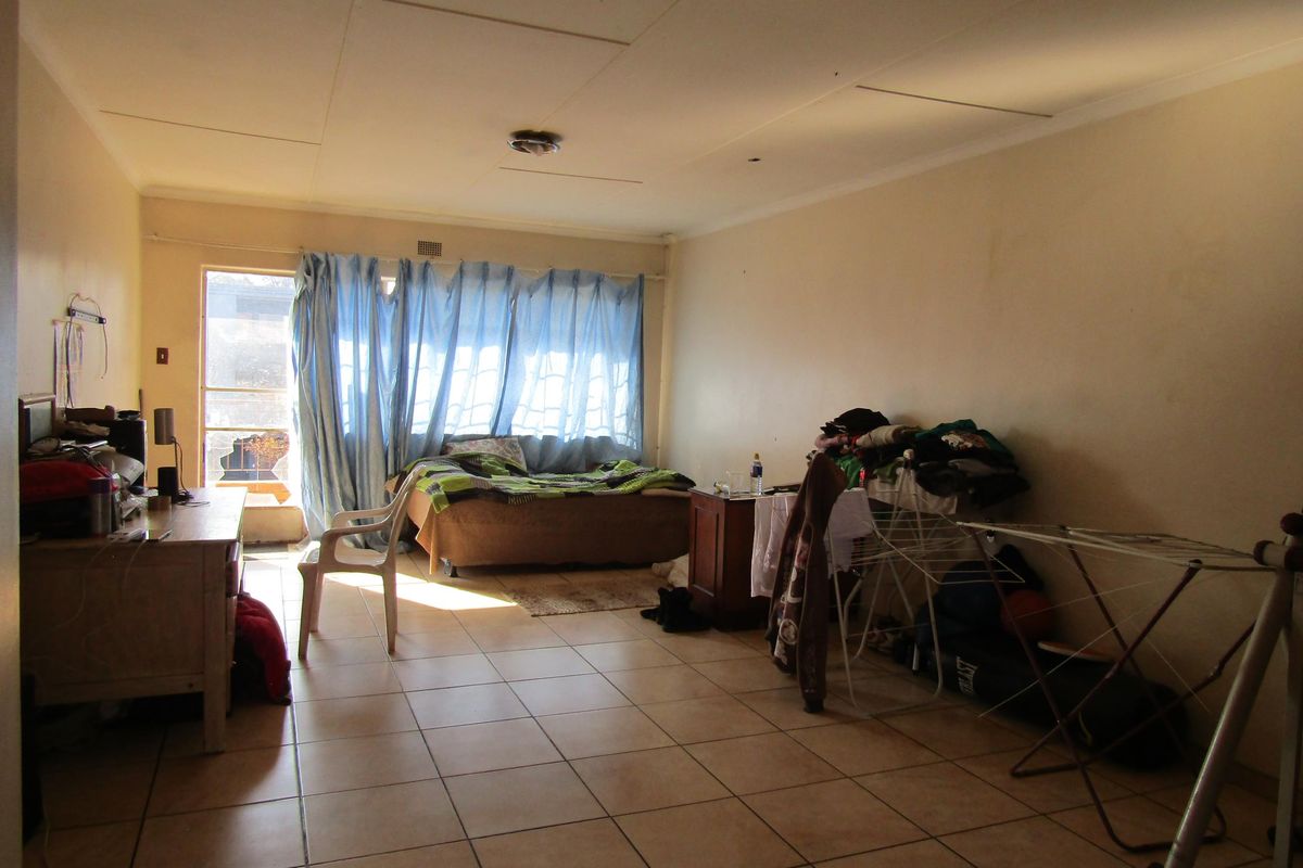 A living room featuring tiled flooring and a sliding glass door leading to an outdoor area, currently showing signs of wear and maintenance needs.
