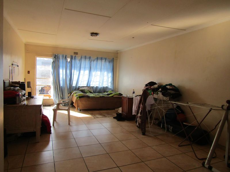 A living room featuring tiled flooring and a sliding glass door leading to an outdoor area, currently showing signs of wear and maintenance needs.