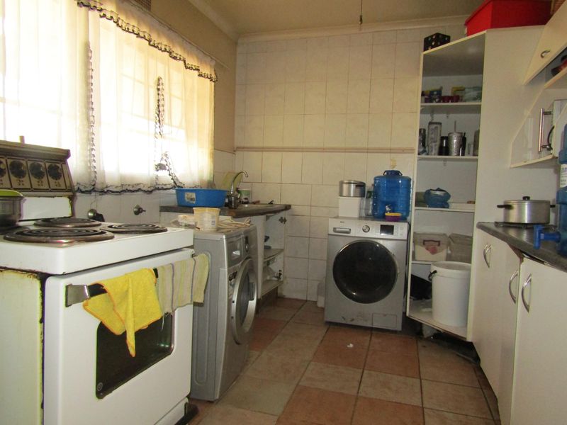 A functional kitchen featuring tiled flooring, a tiled splashback, and built-in cabinetry with space for laundry appliances.