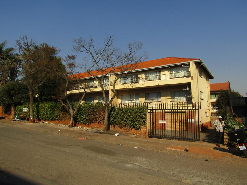 Front elevation of a multi-story apartment building featuring balconies, a tiled roof, and a secure gated entrance.