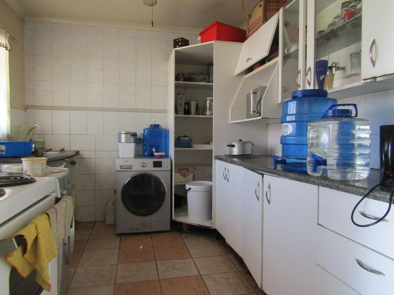A functional kitchen featuring built-in cabinetry, tiled backsplash, and integrated laundry plumbing, offering potential for modernization and aesthetic updates.