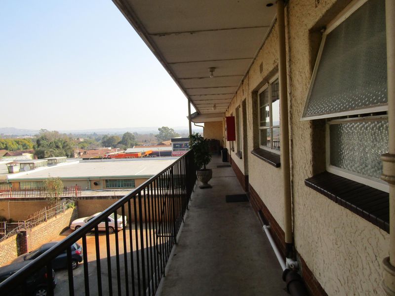 An exterior balcony walkway featuring a metal balustrade, concrete flooring, and views over the surrounding neighborhood.