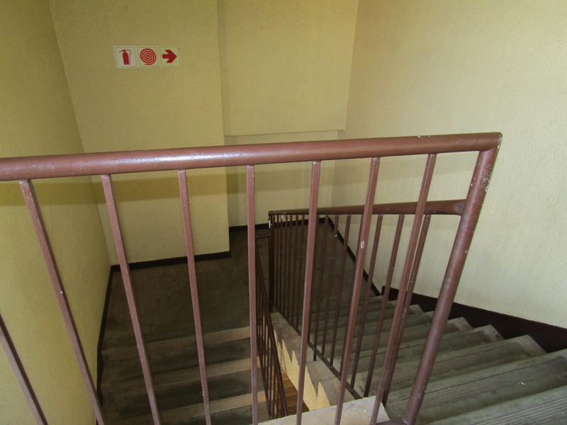 A functional stairwell area featuring a metal balustrade and standard fire safety signage, providing access between apartment levels.