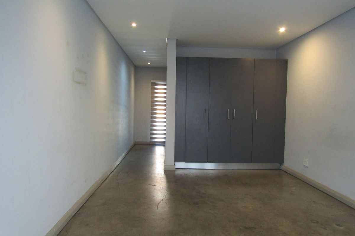 An empty bedroom featuring polished concrete flooring, built-in dark grey cupboards, and recessed downlighting.