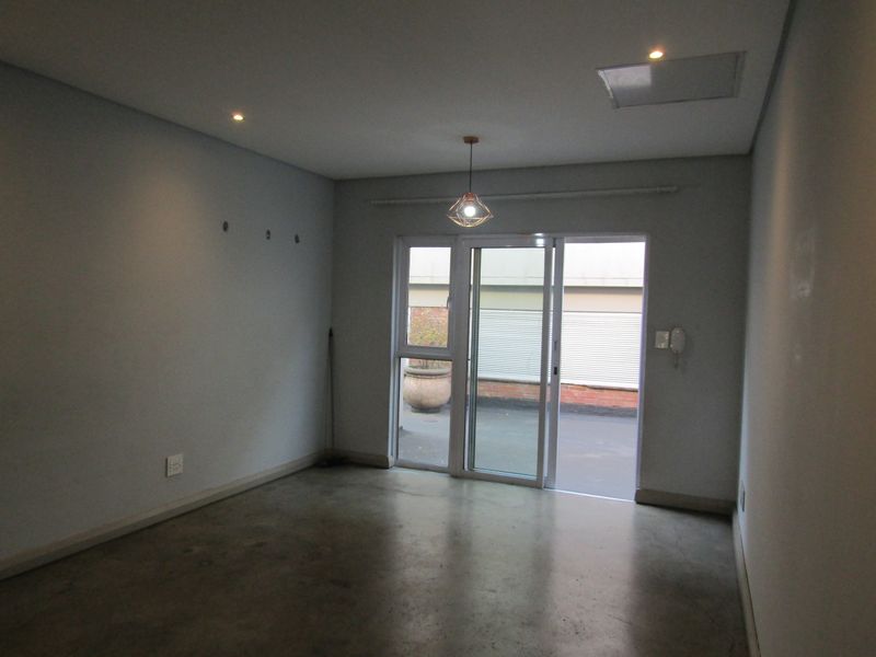 An empty living room featuring polished concrete floors, recessed lighting, and a sliding glass door providing access to an outdoor area.