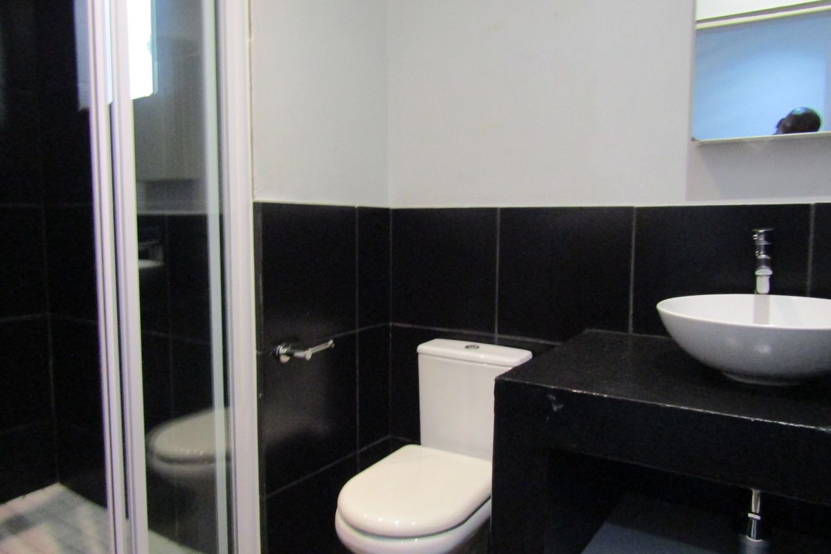 A modern bathroom featuring a shower enclosure, white toilet, and a vessel sink set on a black vanity countertop.