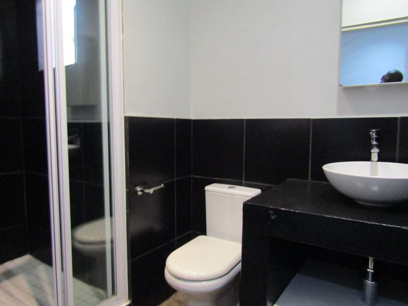 A modern bathroom featuring a shower enclosure, white toilet, and a vessel sink set on a black vanity countertop.