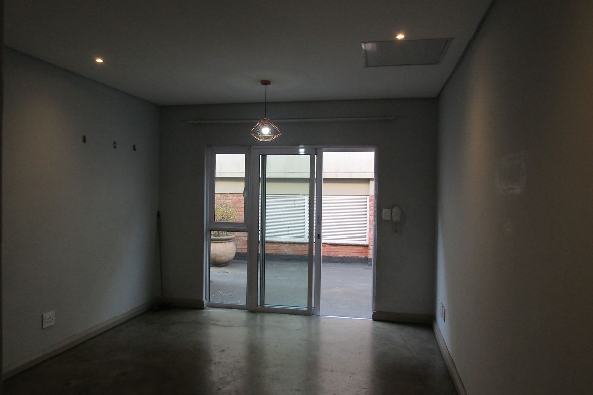 An empty living room featuring concrete flooring, recessed lighting, and a sliding glass door providing access to an outdoor patio area.