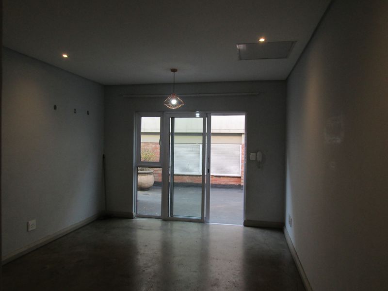 An empty living room featuring concrete flooring, recessed lighting, and a sliding glass door providing access to an outdoor patio area.
