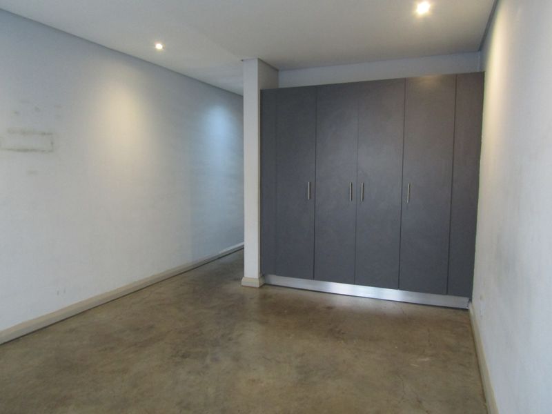 An empty bedroom featuring modern grey built-in cupboards, recessed downlighting, and polished concrete flooring.