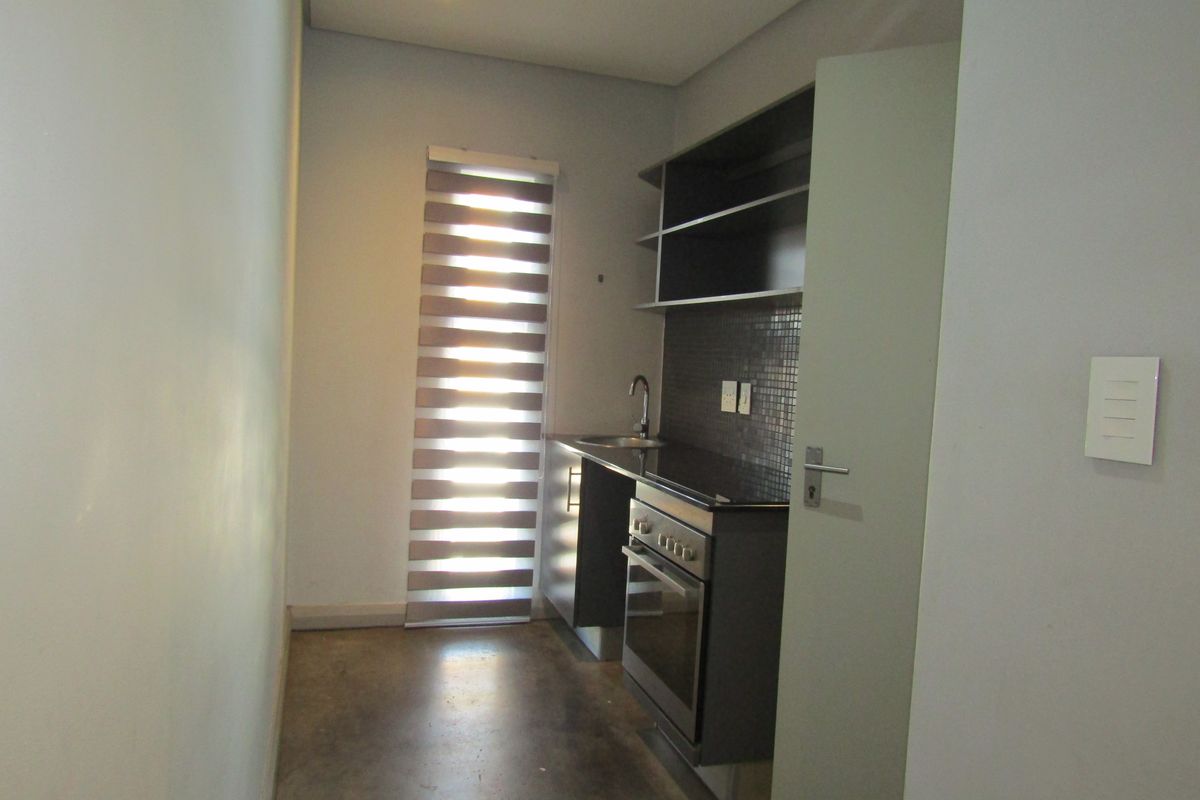 A compact, modern kitchen featuring built-in cabinetry, a stainless steel oven and hob, mosaic tile backsplash, and polished concrete flooring.