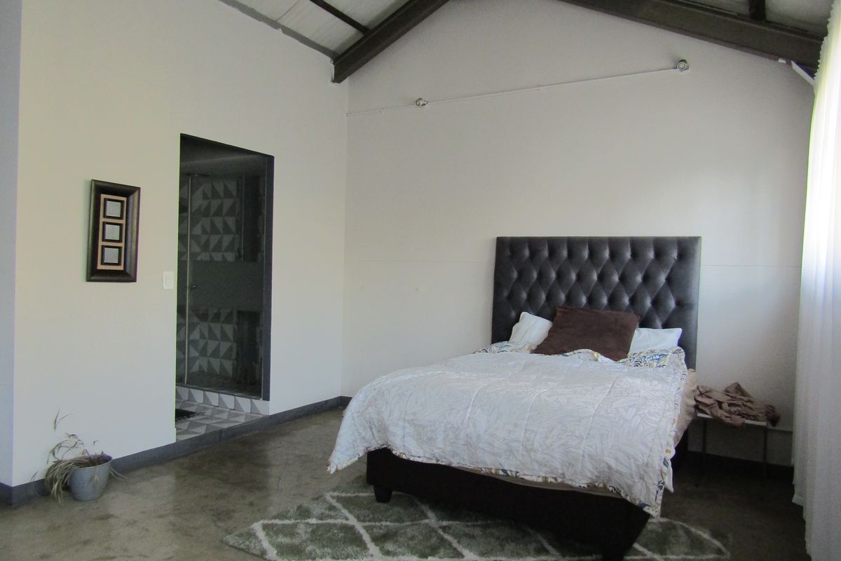 Spacious bedroom featuring high vaulted ceilings with exposed rafters, polished concrete floors, and direct access to an en-suite bathroom.