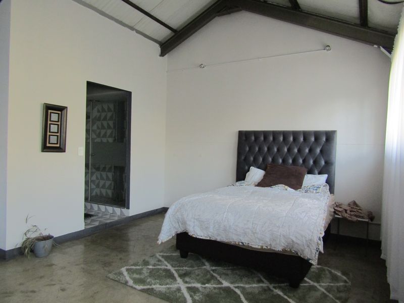 Spacious bedroom featuring high vaulted ceilings with exposed rafters, polished concrete floors, and direct access to an en-suite bathroom.