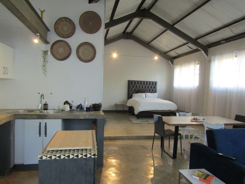 Open-plan studio apartment featuring exposed timber roof trusses, polished concrete floors, and a functional kitchen area with concrete countertops.