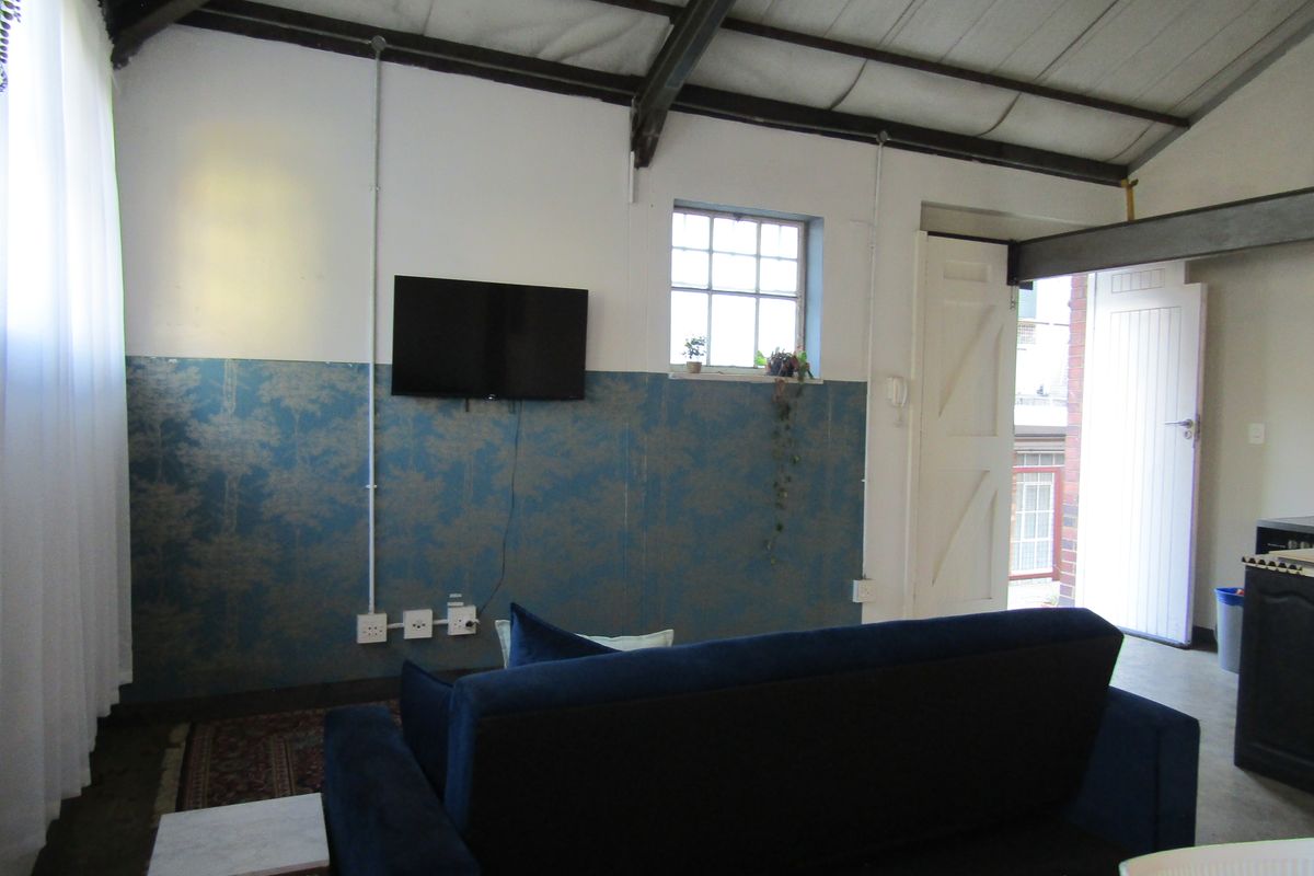 Living area featuring exposed steel roof beams, industrial-style exposed electrical conduit, and a decorative wallpapered feature wall with direct access to an outdoor area.