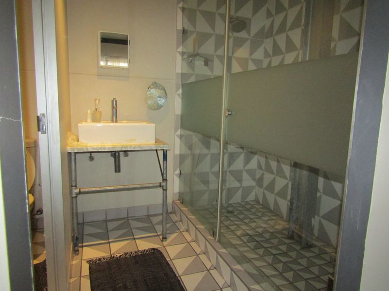 A bathroom featuring a walk-in shower with geometric tiling, a vessel sink on an industrial-style vanity base, and a separate toilet area.