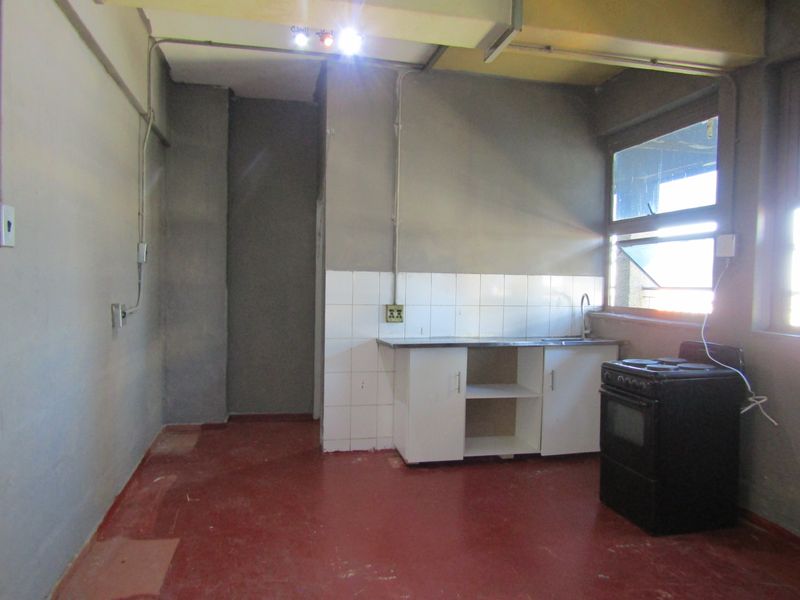 A basic, empty kitchen area featuring a small sink unit, tiled splashback, and exposed electrical conduit, requiring significant cosmetic updates and finishing.