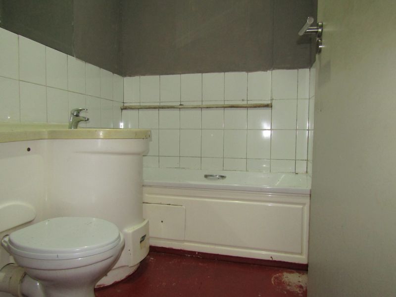 A dated bathroom featuring a standard bathtub, toilet, and basin with wall tiling, requiring renovation to update the finishes and fixtures.