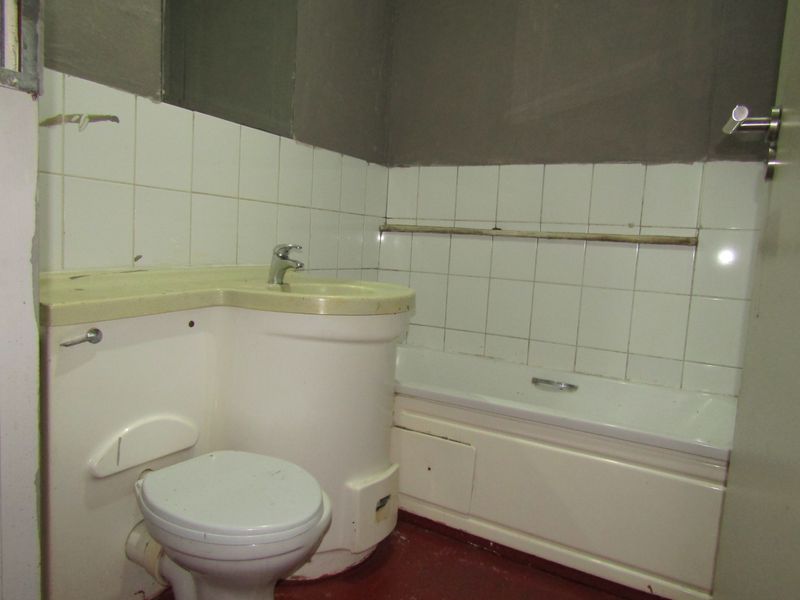A dated bathroom featuring an integrated vanity unit, bathtub, and toilet, currently requiring renovation and finishing of the wall surfaces.