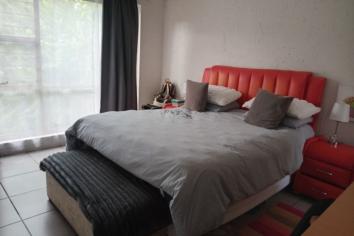 A bedroom featuring tiled flooring and a large window with curtain tracks, providing natural light. The space has a textured wall finish.