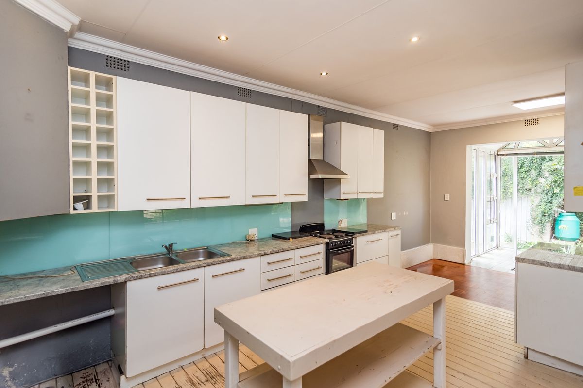 A functional kitchen featuring white cabinetry, a stainless steel extractor fan, a glass splashback, and a central island, with direct access to the rear garden.