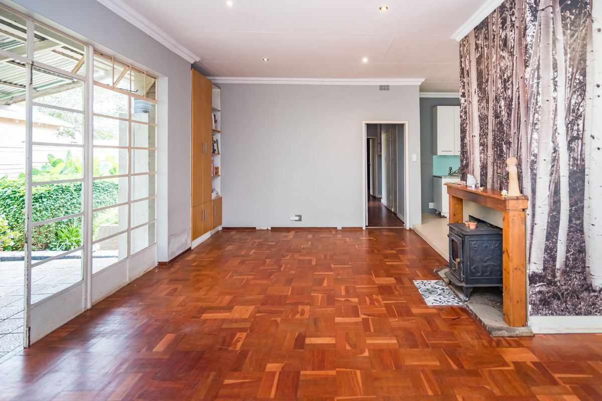 Spacious living area featuring original parquet flooring, a built-in fireplace with decorative surround, and large glass sliding doors opening to the garden.