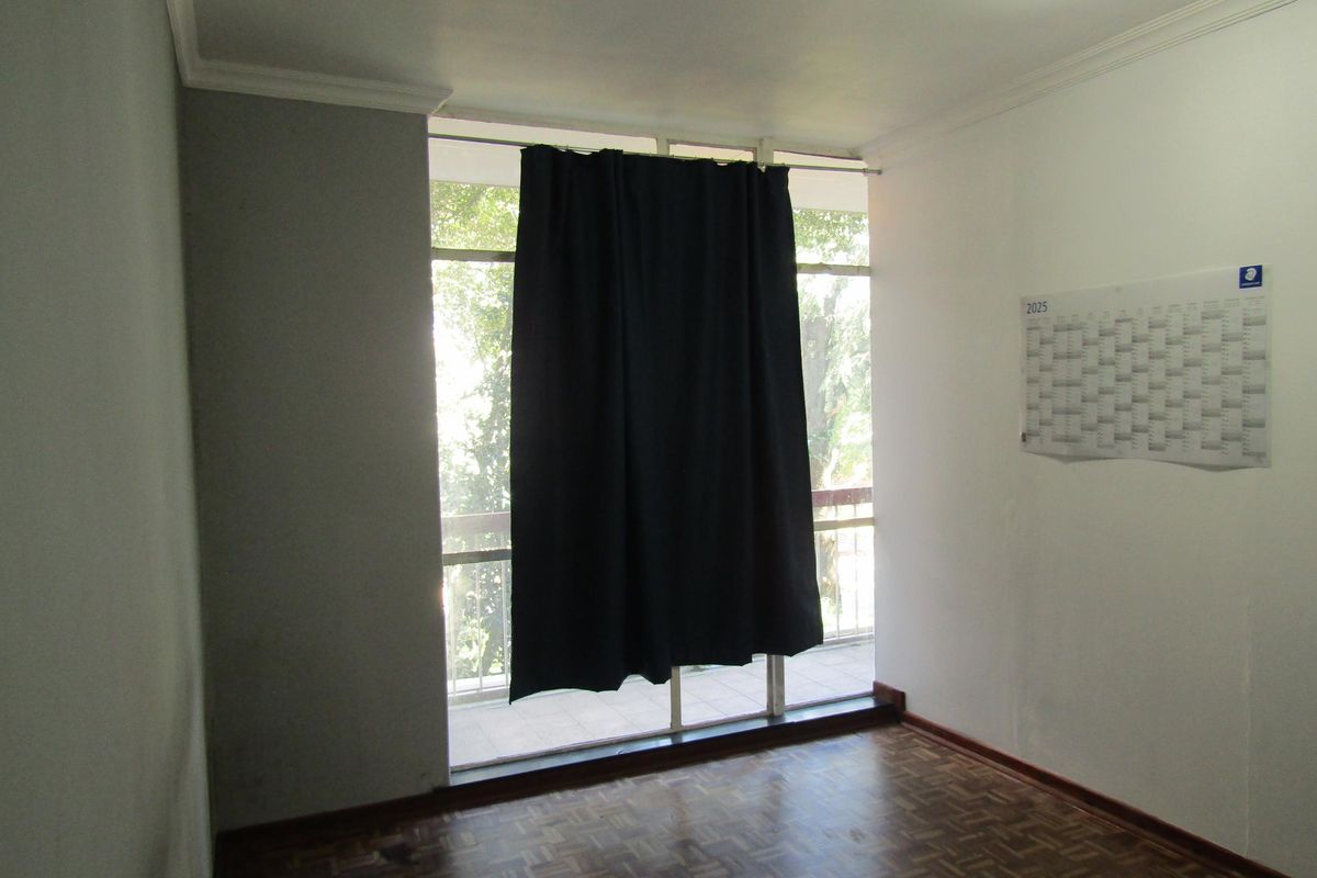 A simple bedroom featuring parquet flooring, large floor-to-ceiling windows, and access to an attached balcony.