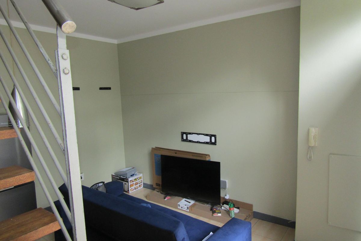 A living area featuring tiled flooring, a staircase with a metal railing, and wall-mounted fixtures.