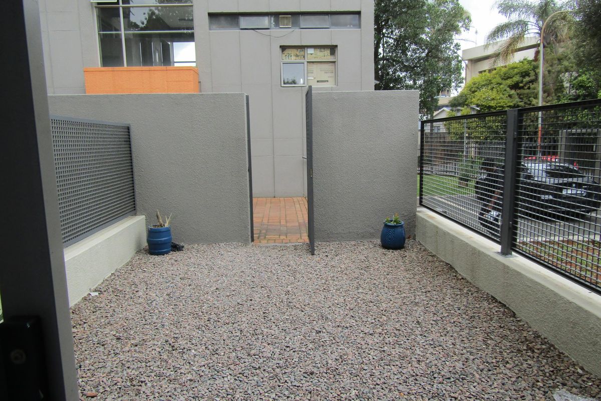 A private outdoor courtyard area featuring gravel surfacing, enclosed by a combination of solid masonry walls and metal mesh fencing.