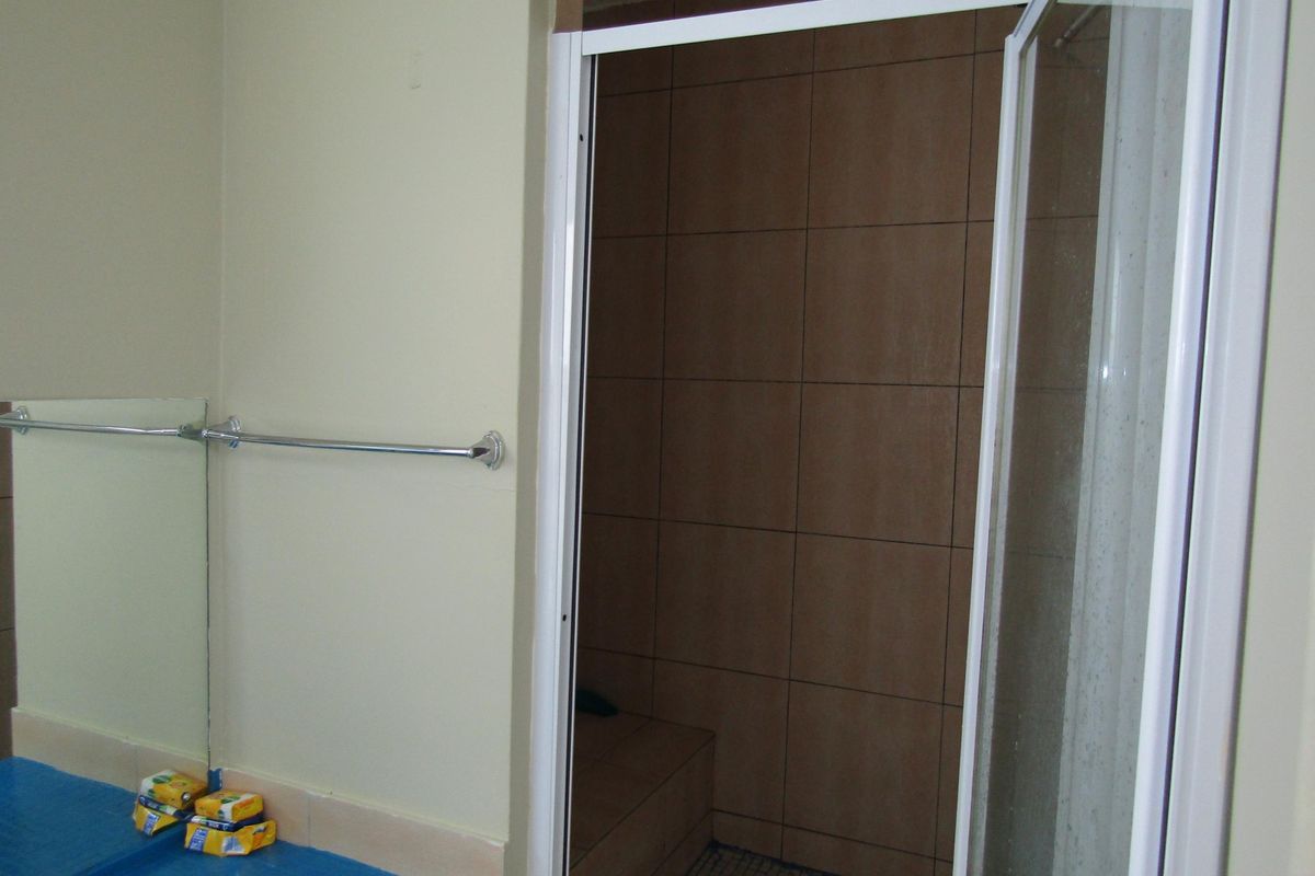 A functional bathroom featuring a walk-in shower with brown tiled walls and a white framed glass door, complemented by a wall-mounted towel rail.