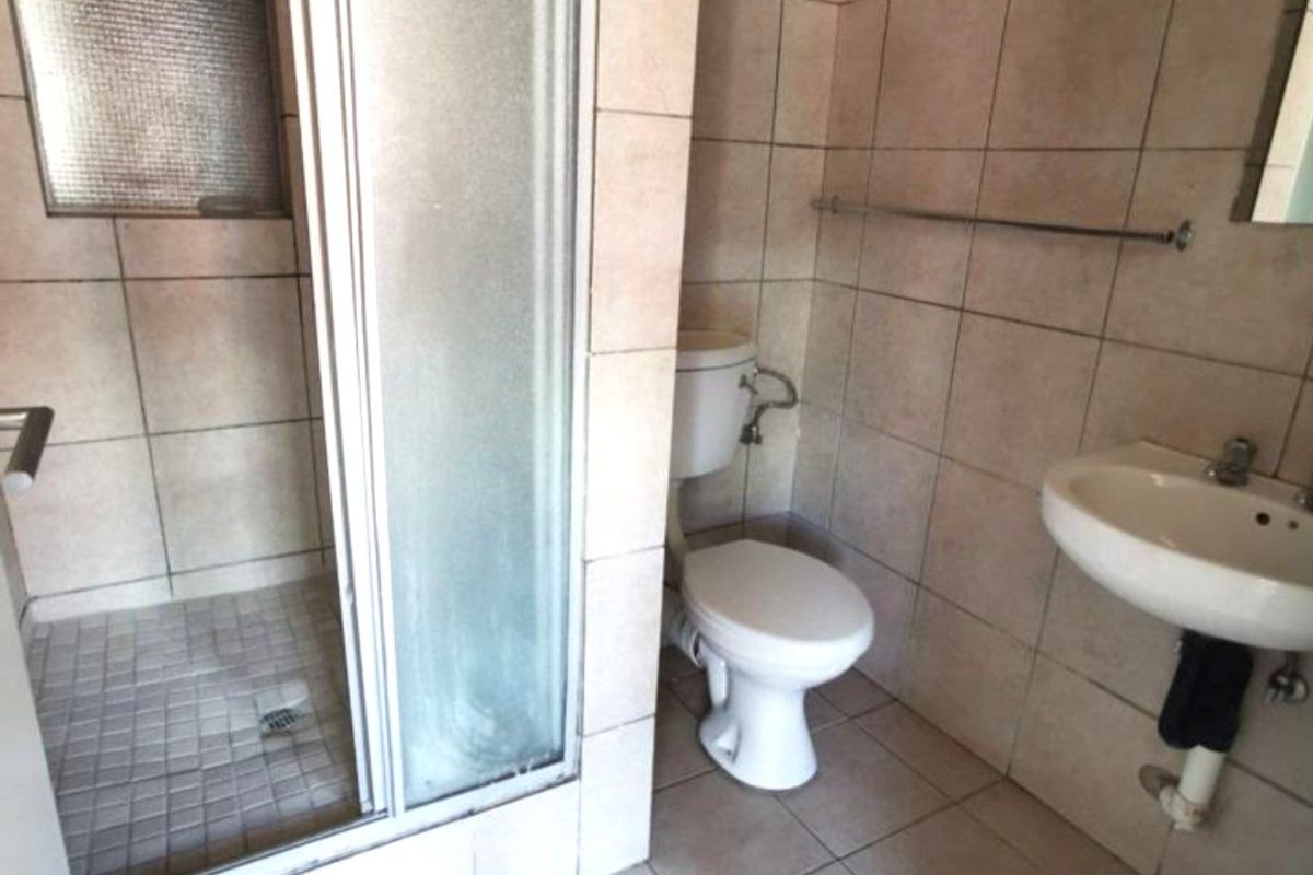 A functional bathroom featuring a glass-enclosed shower, a wall-mounted basin, and a standard toilet with neutral floor and wall tiling.