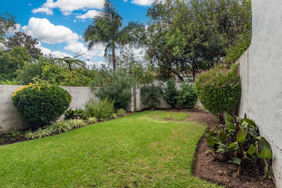 A private rear garden featuring a well-maintained lawn, established perimeter shrubbery, and high boundary walls for added privacy.