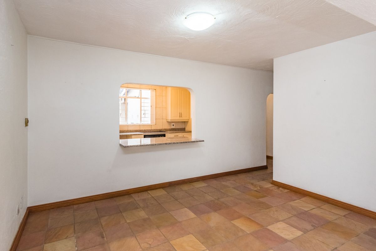 An empty living area featuring tiled flooring and a service hatch opening into the kitchen, creating an open-plan feel.