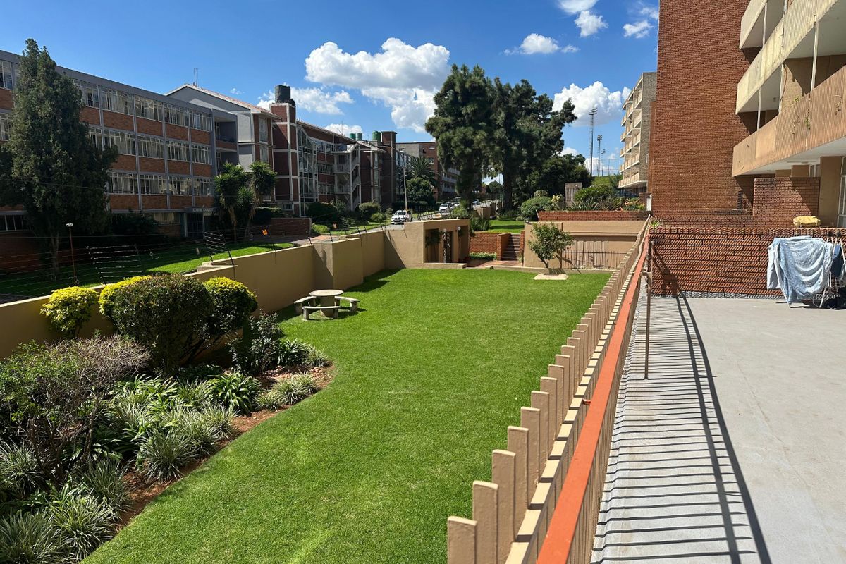 A view of the communal garden area and surrounding apartment complex buildings, featuring well-maintained lawn and perimeter fencing.