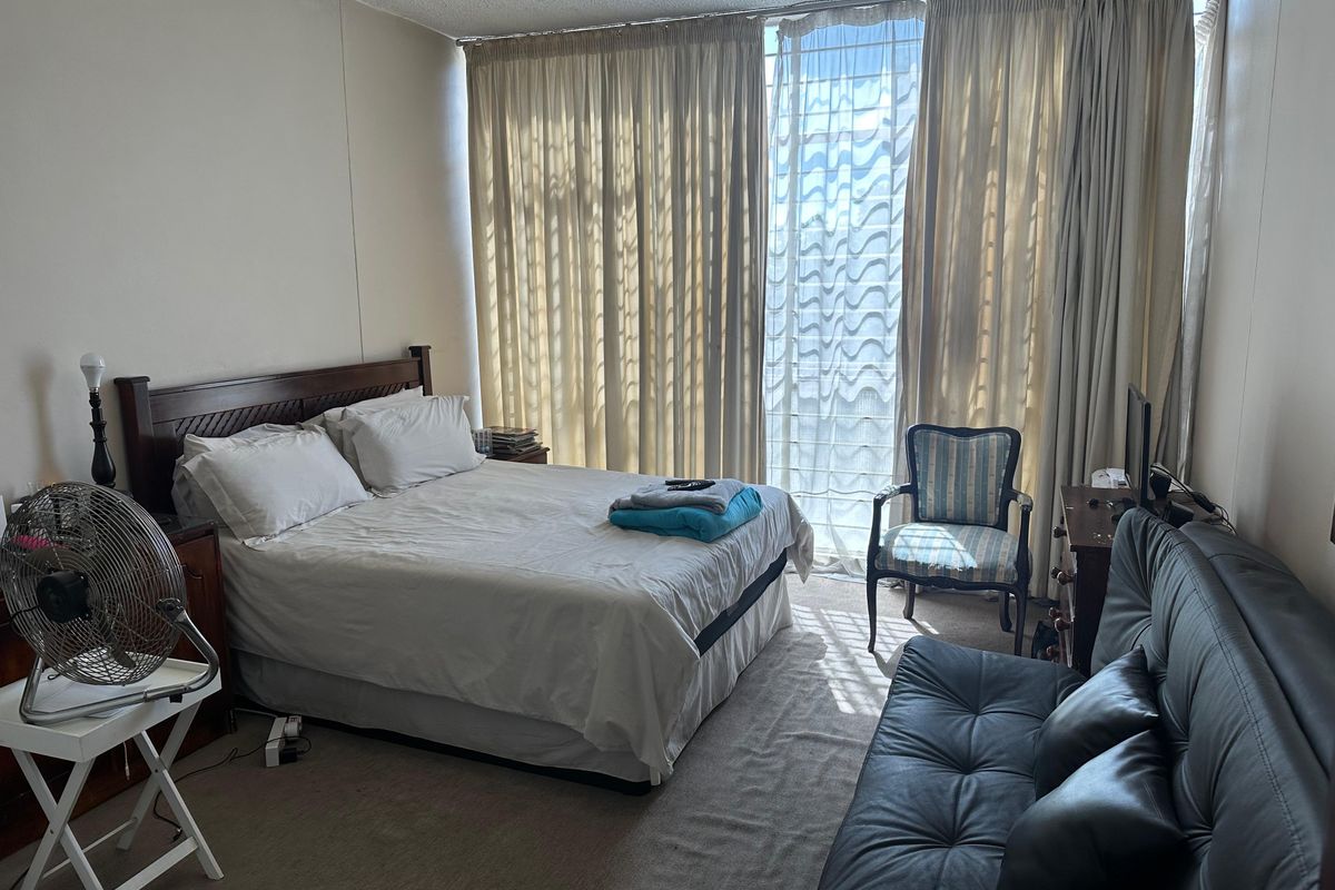 A spacious bedroom featuring neutral wall finishes, carpeted flooring, and large floor-to-ceiling windows that provide ample natural light.