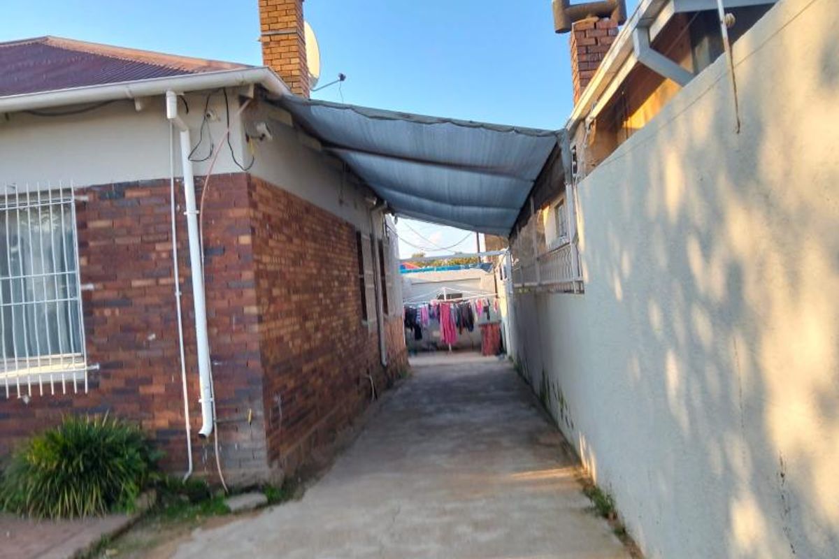 Side passage of the property featuring a concrete walkway, brick exterior walls, and a covered outdoor area with a shade cloth structure.