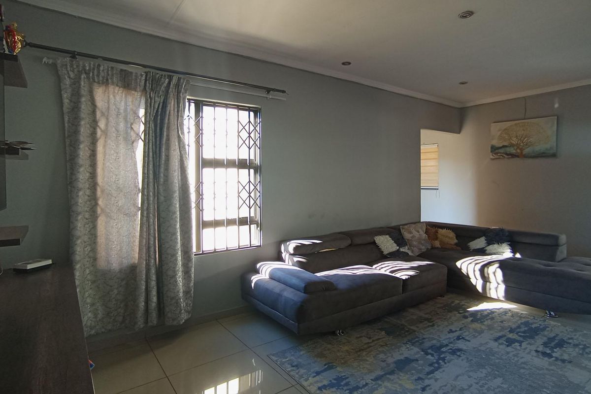A spacious living room featuring tiled flooring, recessed ceiling lighting, and security bars on the windows.