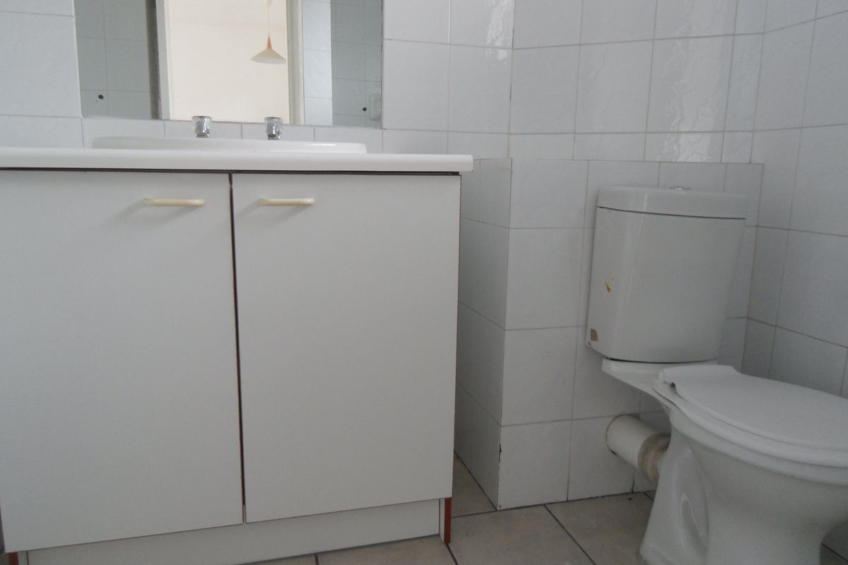 A functional bathroom featuring a white vanity cabinet with integrated basin, wall-mounted mirror, and a standard toilet suite with full-height wall tiling.