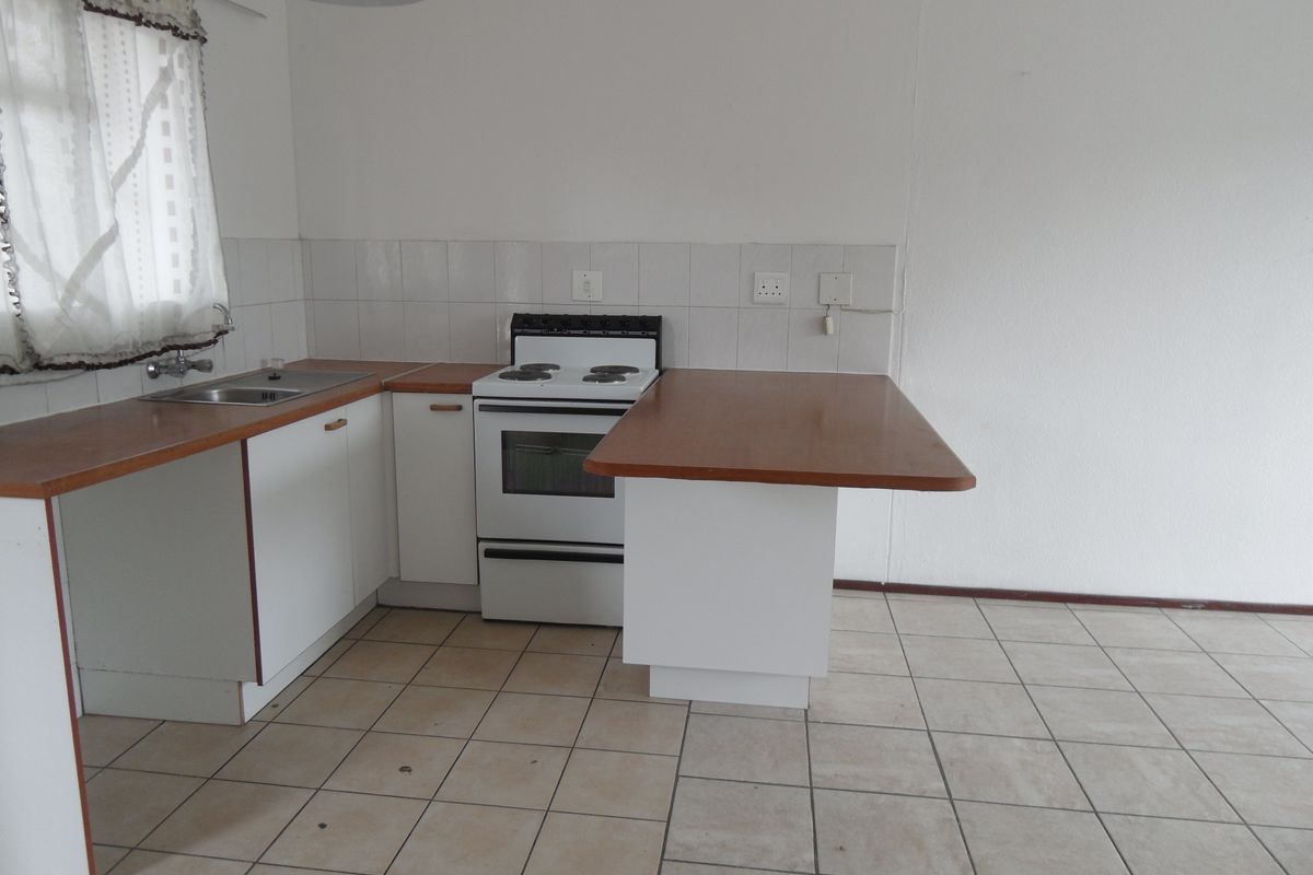 A dated kitchen featuring white cabinetry, a freestanding stove, tiled splashbacks, and a breakfast counter, requiring cosmetic updates to modernize the space.