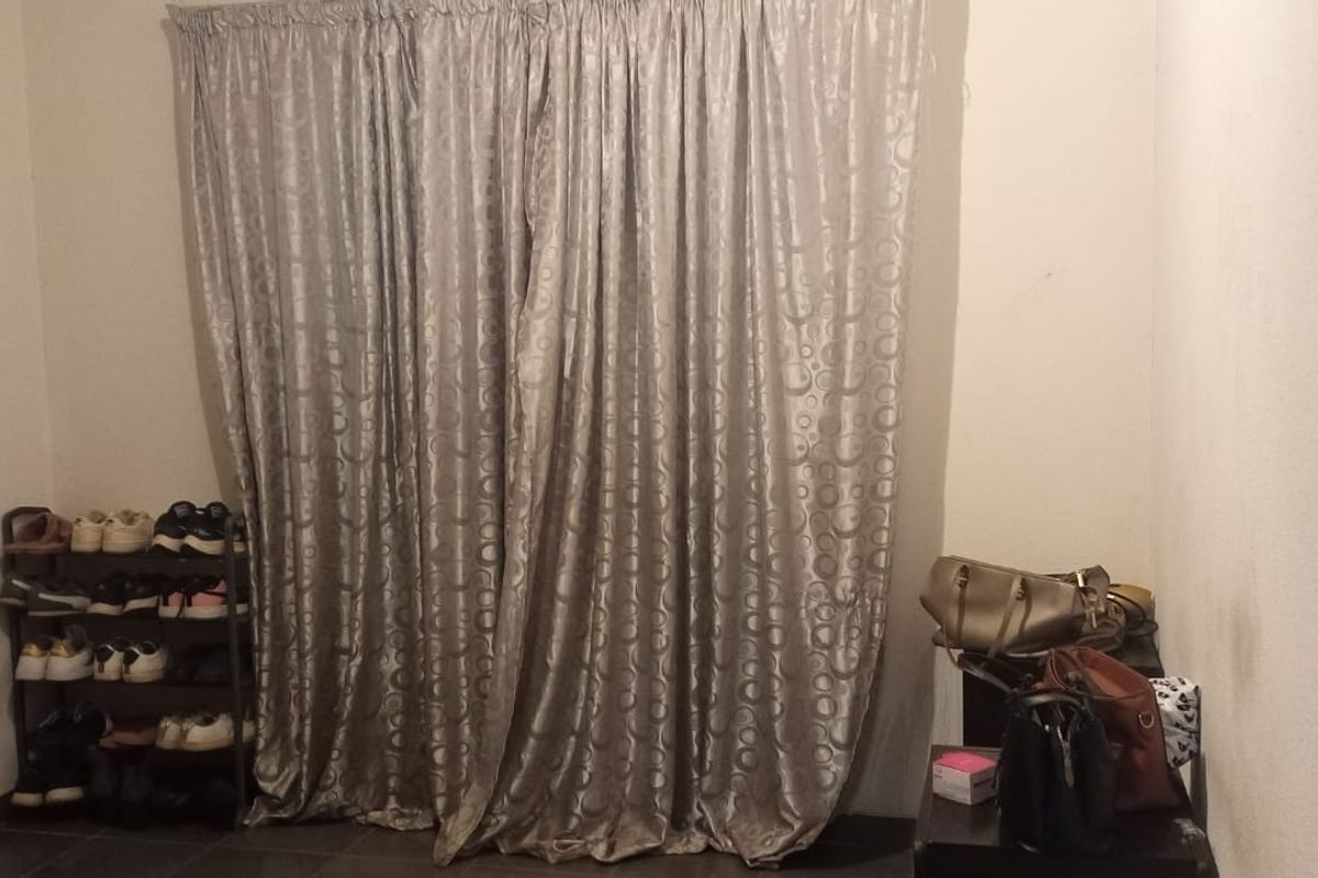 A bedroom interior featuring tiled flooring and full-length curtains covering the window area.