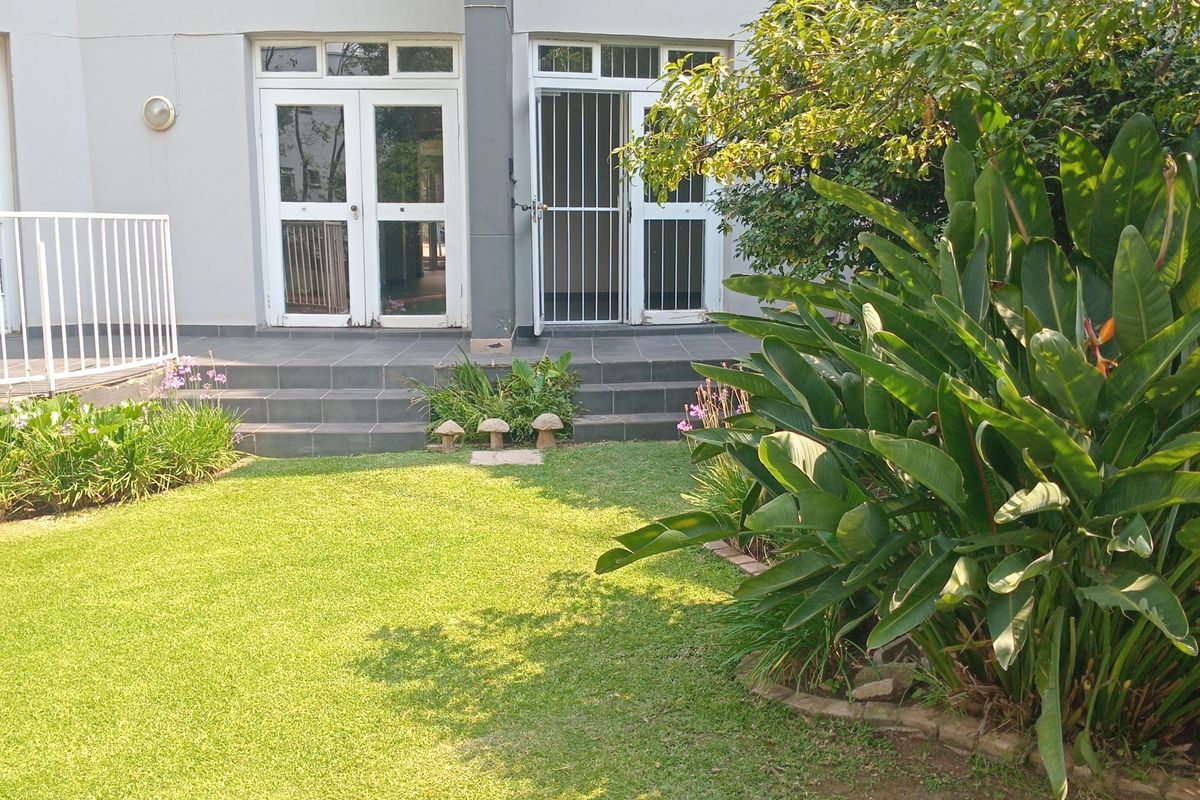 A view of the apartment's rear exterior, featuring a private garden, paved patio area, and direct access through double glass doors.