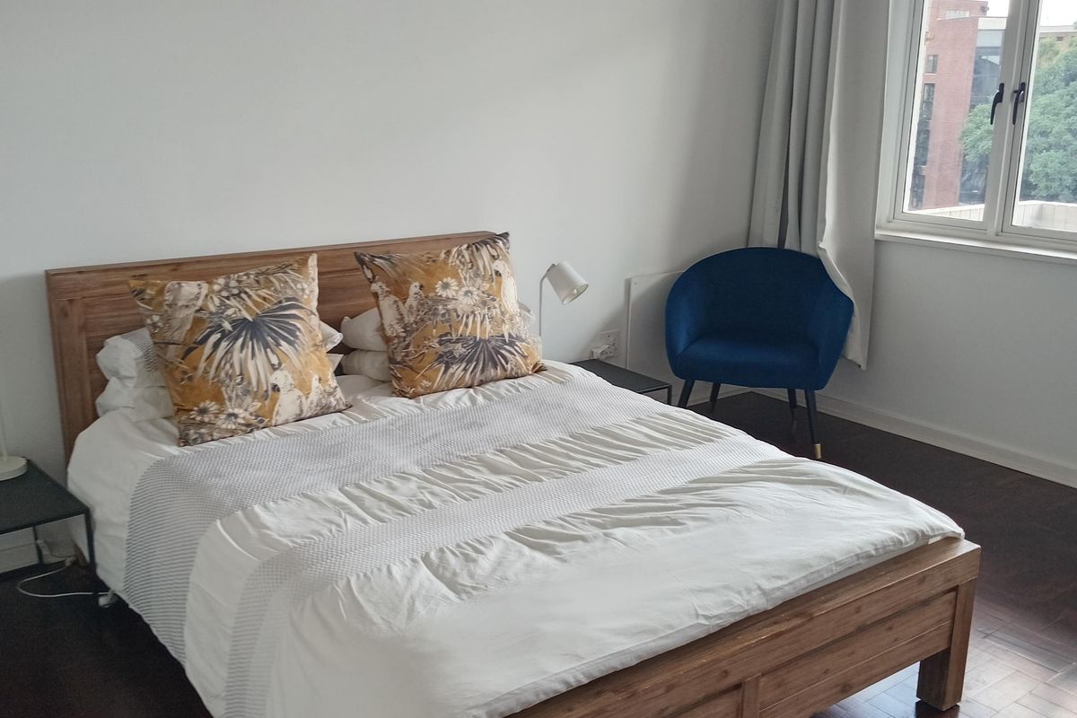 A bright bedroom featuring dark wood parquet flooring and a large window allowing for natural light.